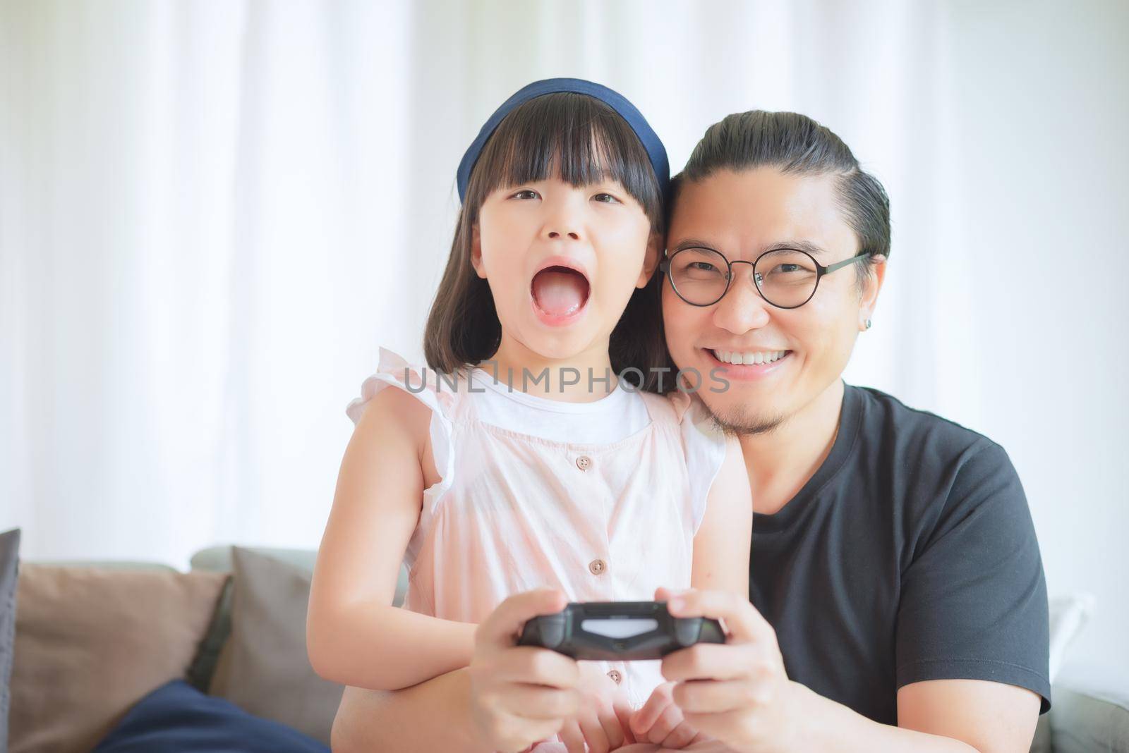 Asian Father and cute daughter enjoy and play console game on vacation at home by Nuamfolio