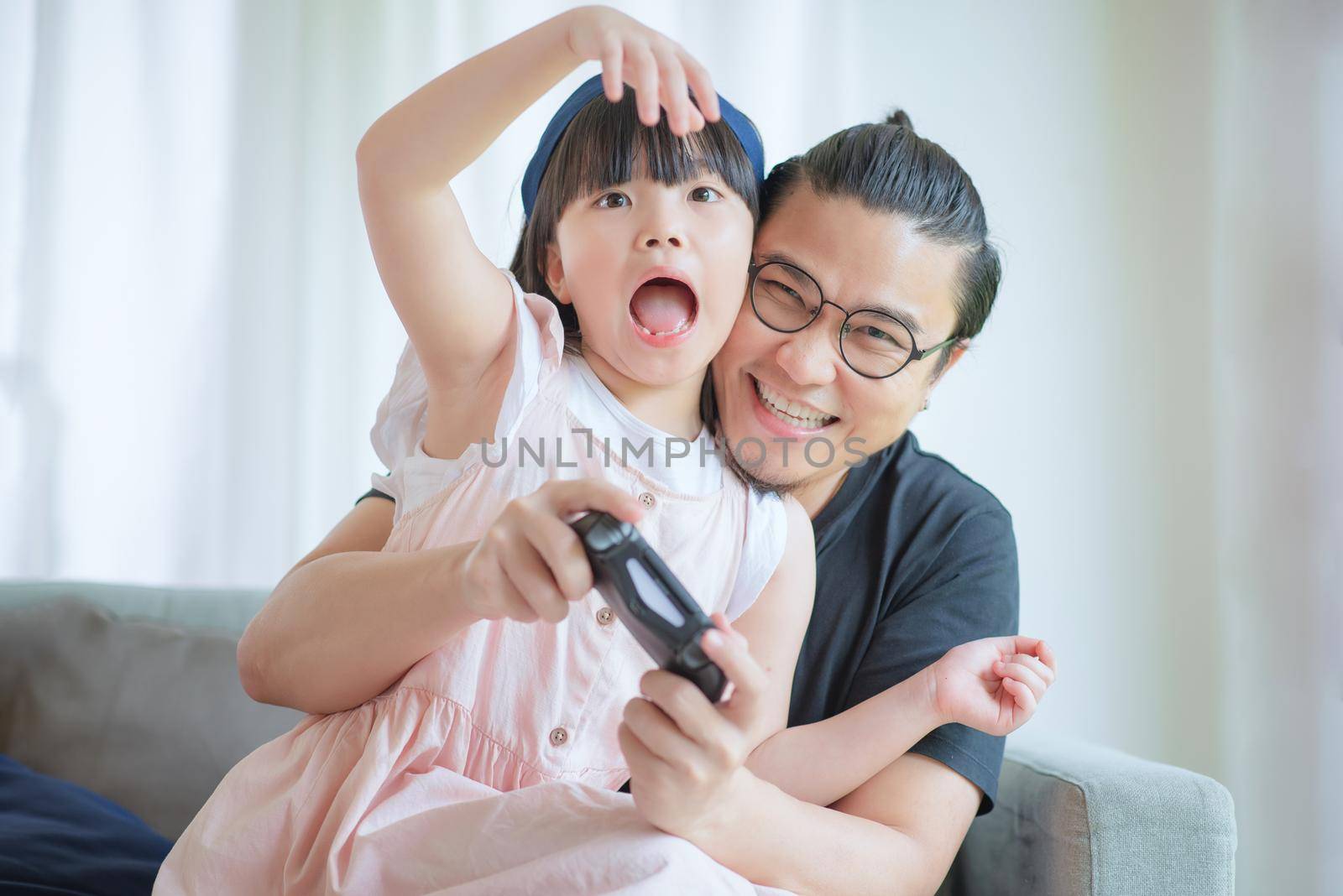 Asian Father and cute daughter enjoy and play console game on vacation at home by Nuamfolio