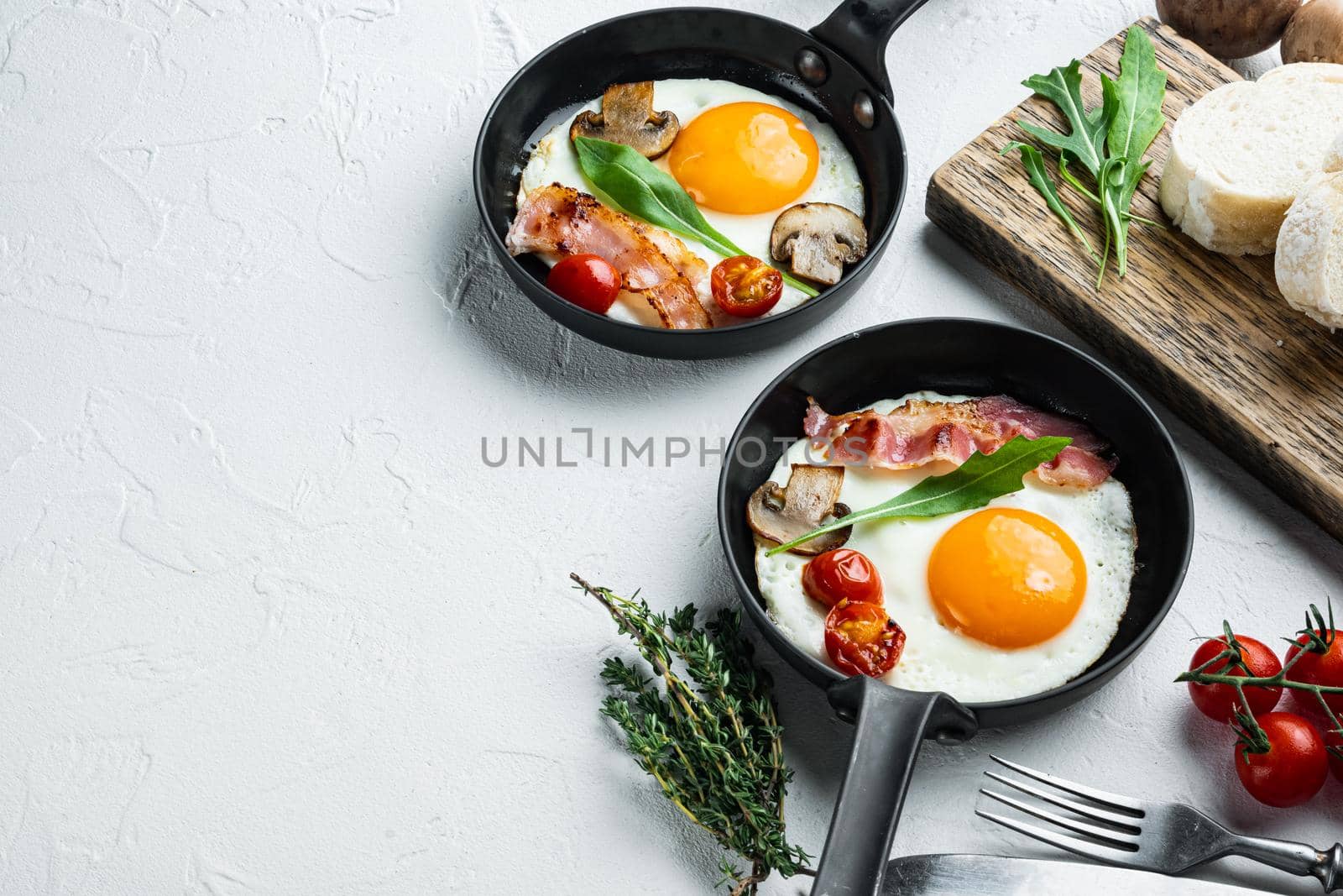 Fried eggs with cherry tomatoes and bread for breakfast in cast iron frying pan, on white background , with space for text copyspace