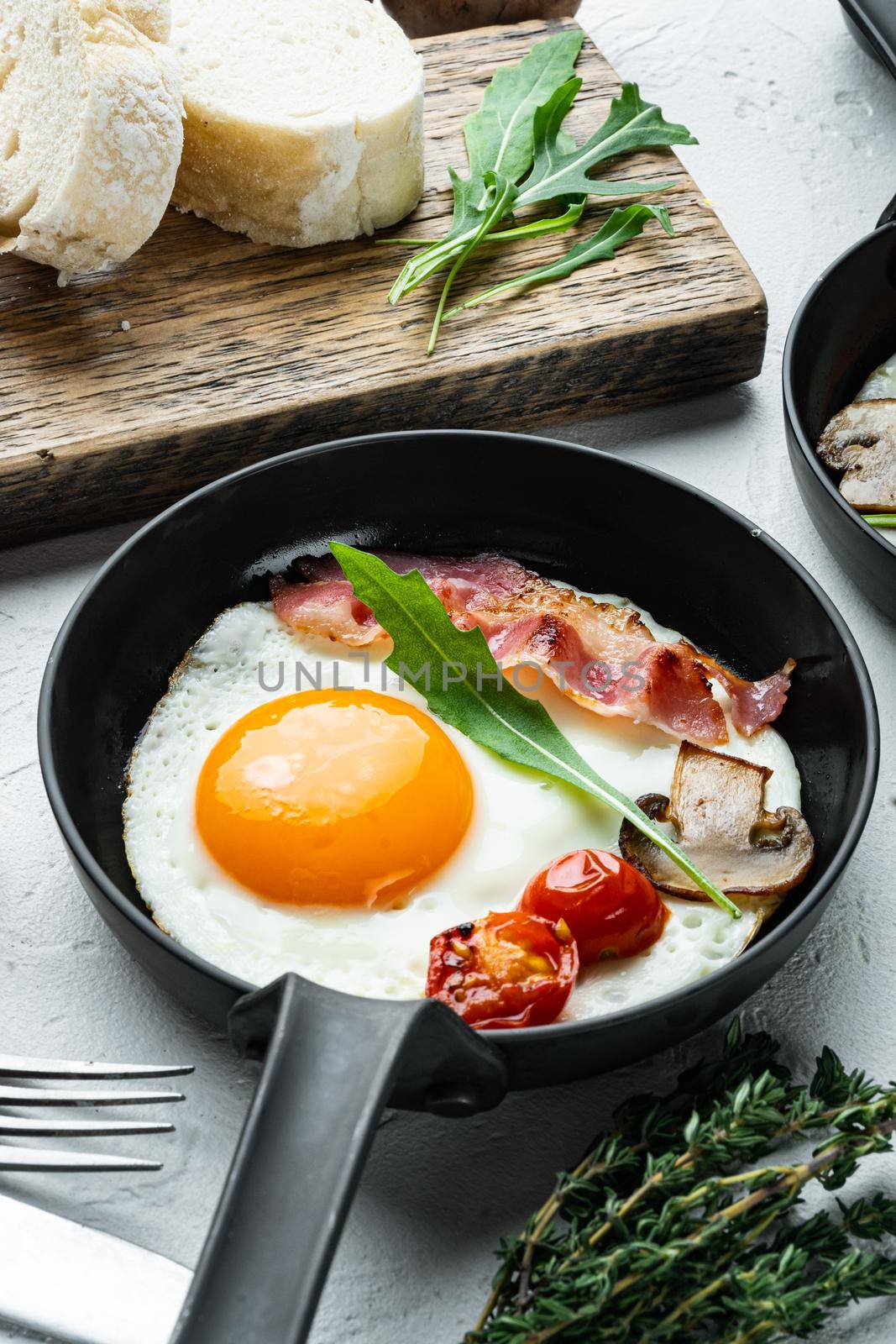 Fried eggs with bacon and vegetables set in cast iron frying pan, on white background