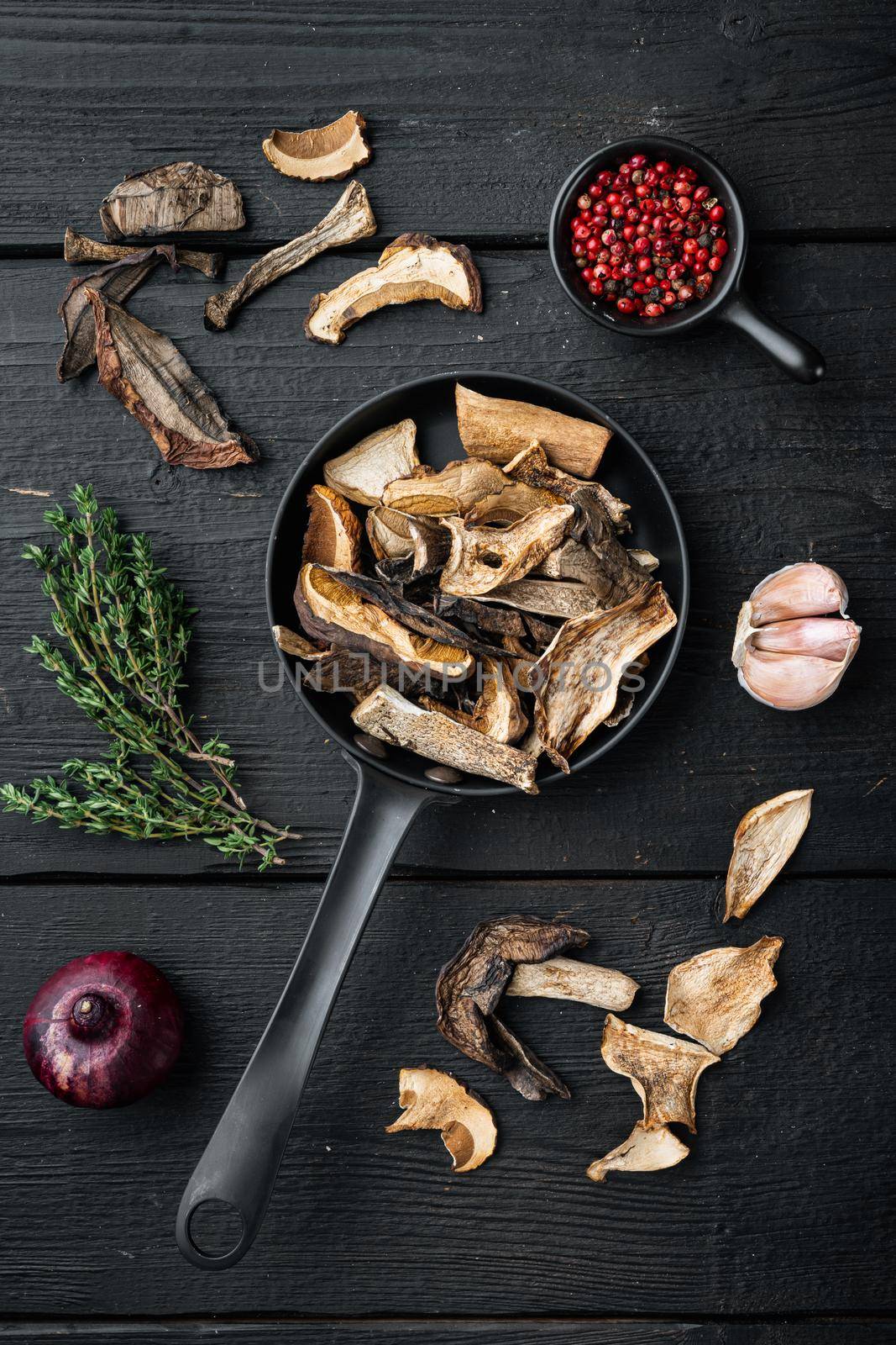 Dried porcini mushrooms set in cast iron frying pan, on black wooden table background, top view flat lay