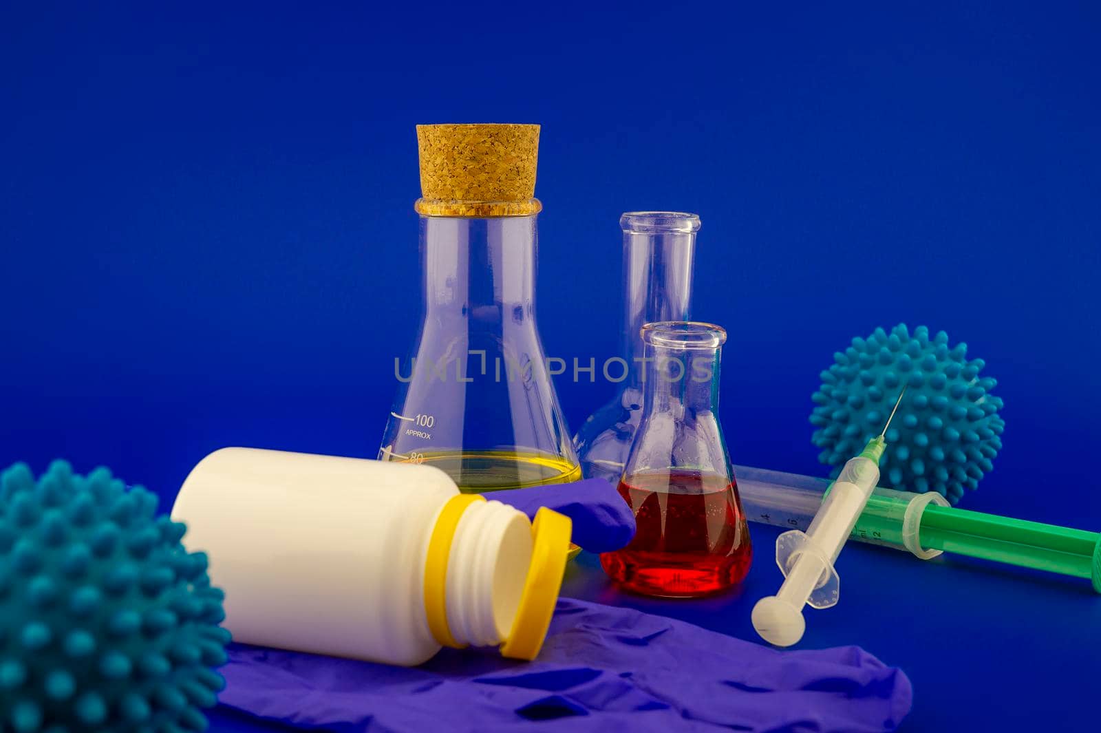 Concept of research for a Covid-19 vaccine with a conical lab flasks with yellow and red solutions alongside a hypodermic syringe and blue virus molecules over a blue background with copy space
