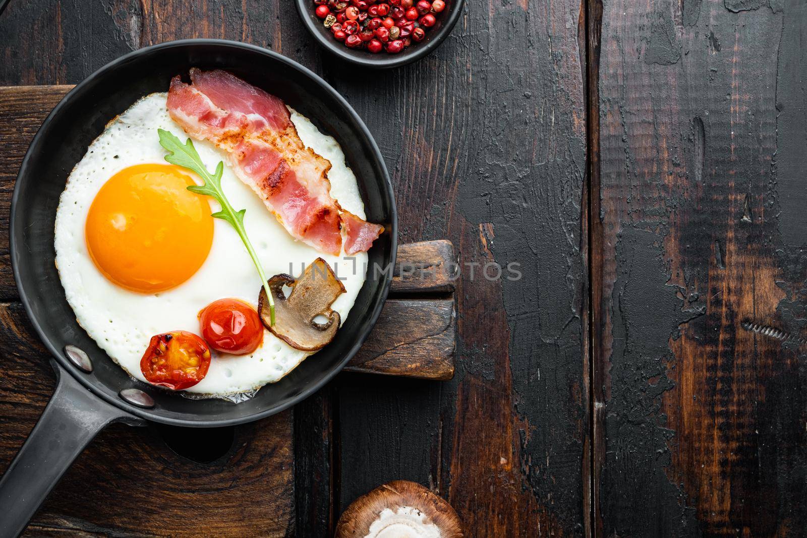 Scrambled eggs in frying pan with pork lard, bread and green feather in cast iron frying pan, on old dark wooden table background, top view flat lay , with space for text copyspace