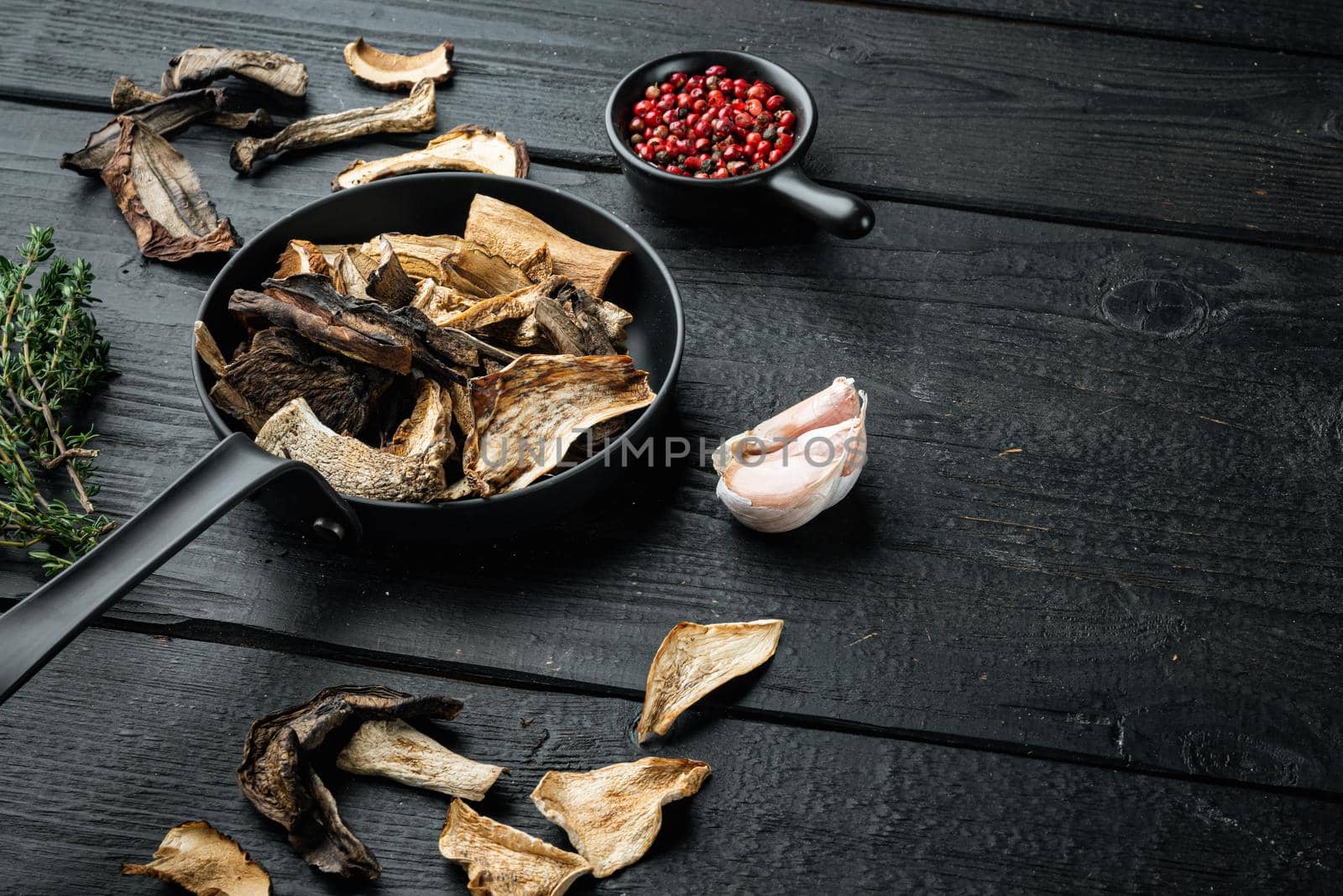 Dried wild mushrooms set in cast iron frying pan, on black wooden table background , with space for text copyspace