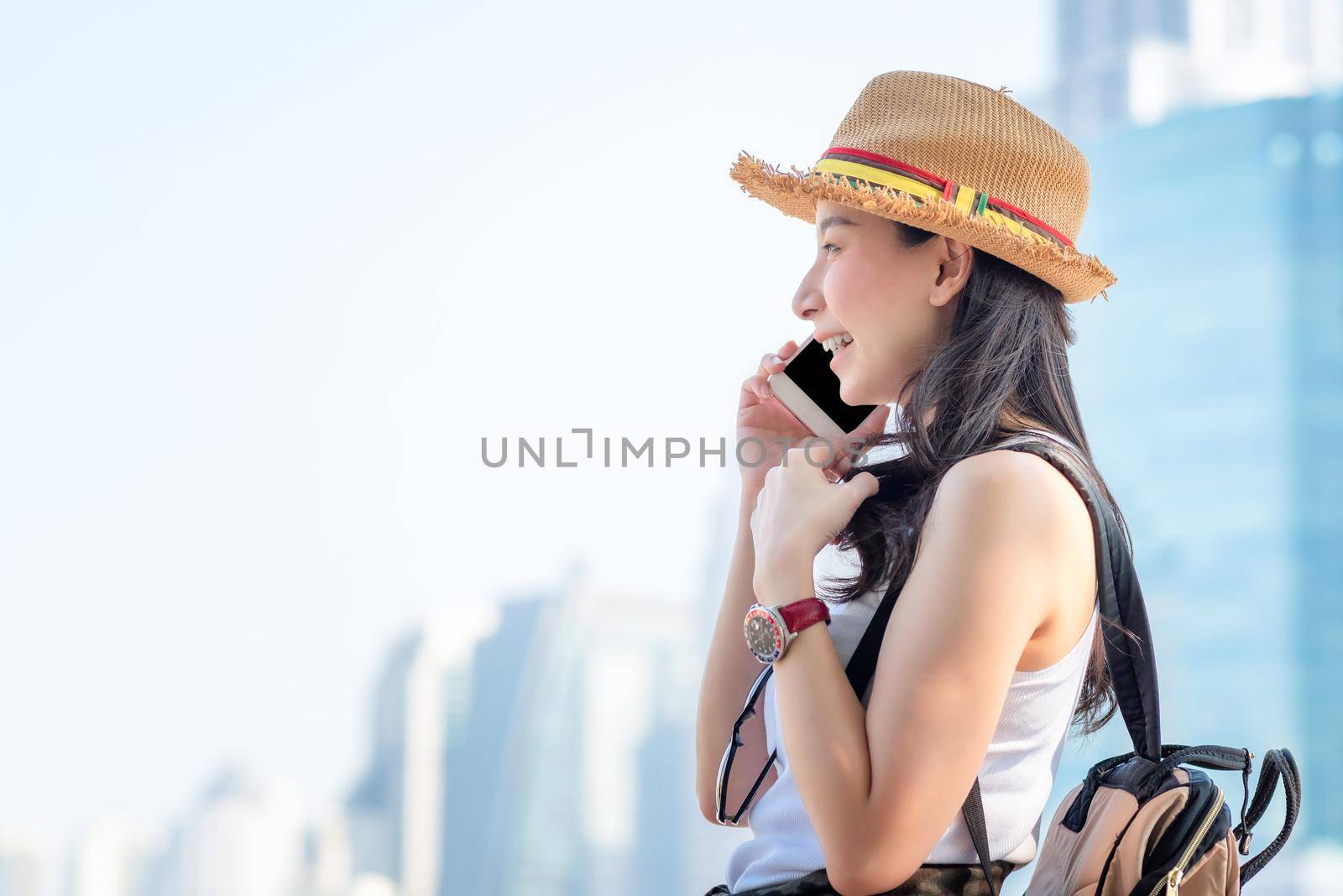 Beautiful asian solo tourist woman smiling and enjoy talking via mobile phone in city downtown. Vacation travel in summer.