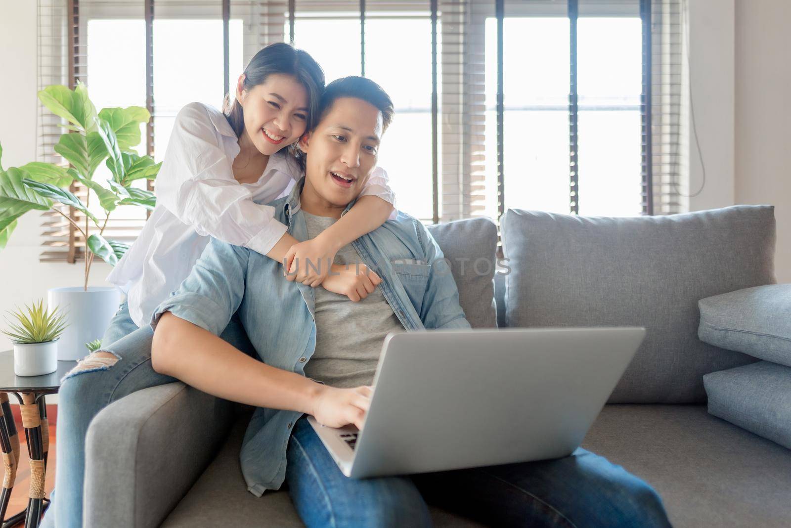 Asian couple lovers enjoy watching online streaming via computer laptop at home by Nuamfolio