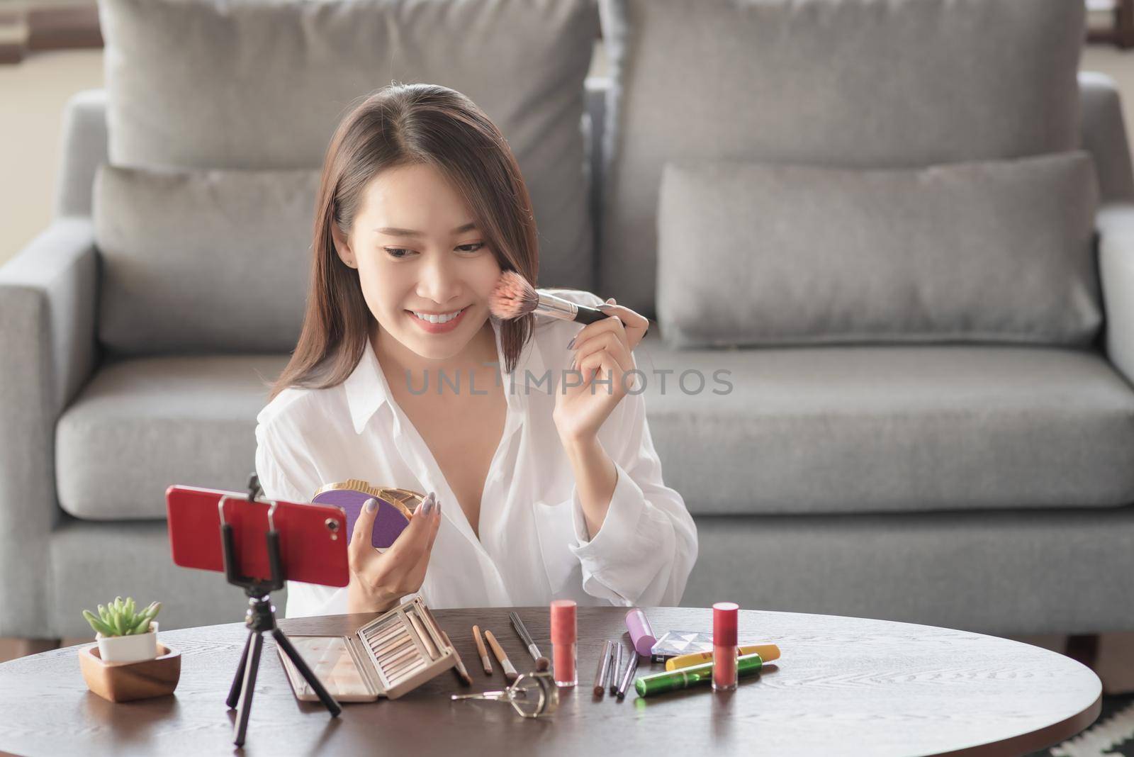 Young female beauty influencer making a video tutorial for her beauty channel on cosmetics during stay safe at home by Nuamfolio