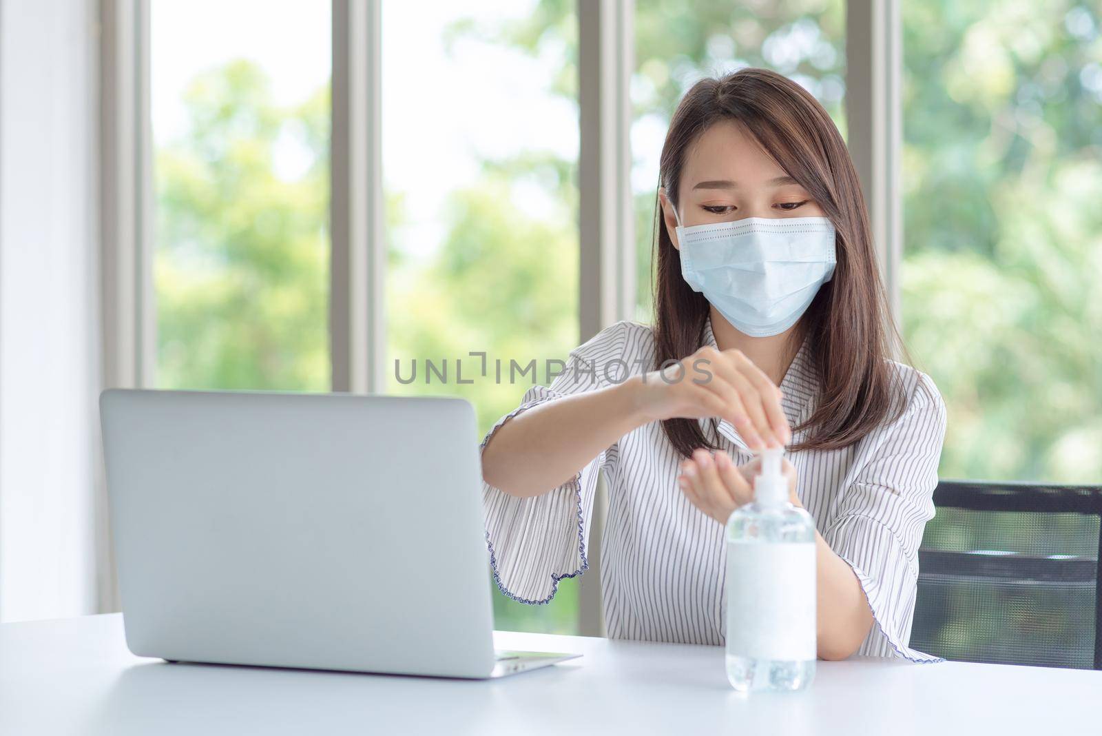 Business woman wearing mask and using personal sanitizer to cleaning her hand in office to keep hygiene by Nuamfolio