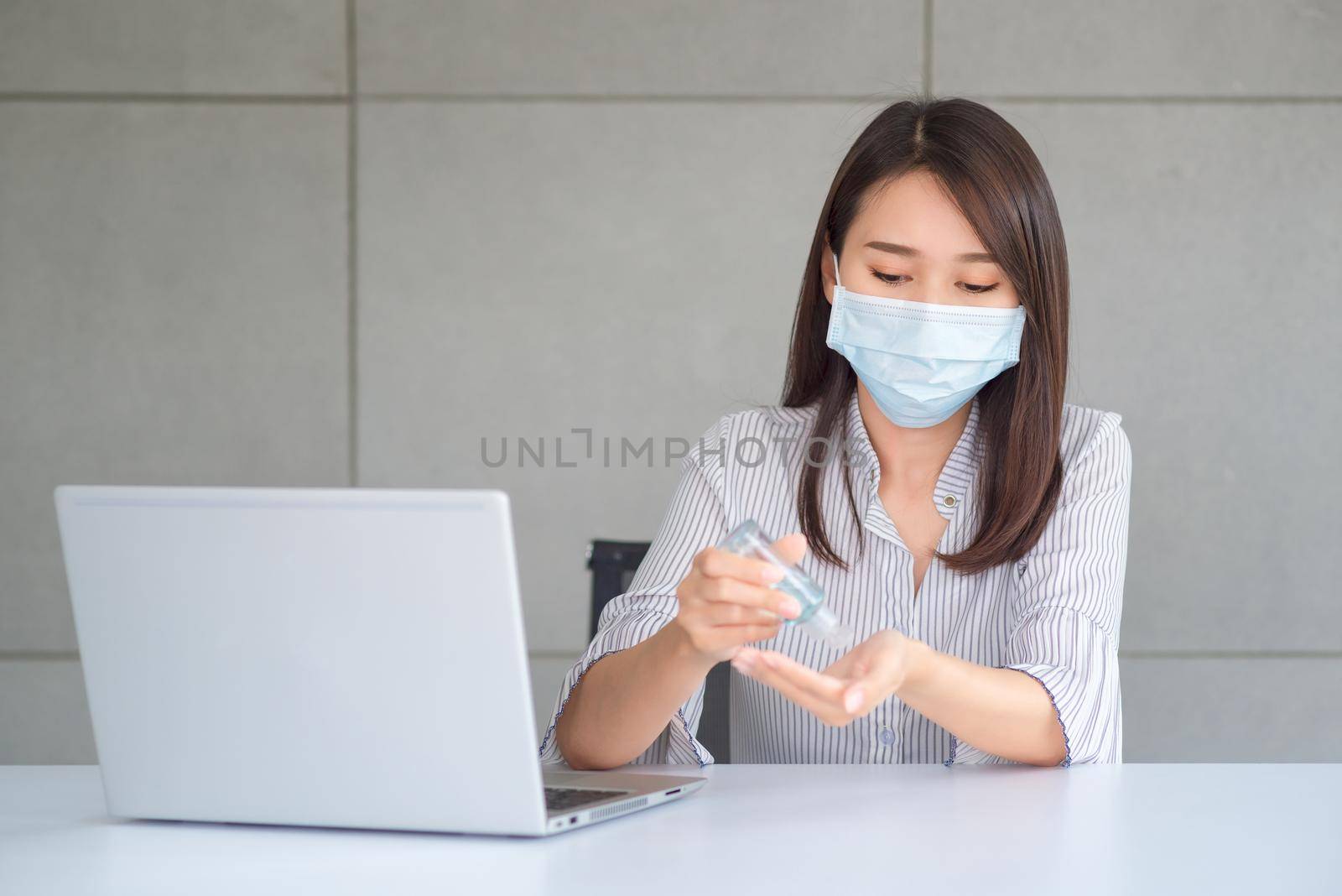 Business woman wearing mask and using personal sanitizer to cleaning her hand in office to keep hygiene. by Nuamfolio