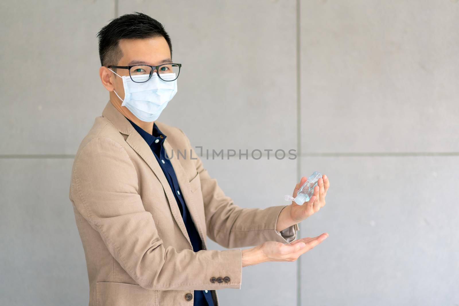 Business man wearing mask and using personal sanitizer to cleaning his hand in office to keep hygiene by Nuamfolio