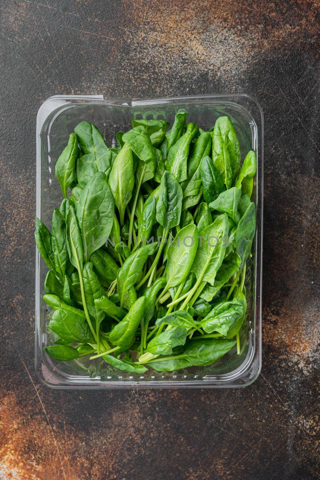 Washed fresh mini spinach set, on old dark rustic background, in plastic pack, top view flat lay