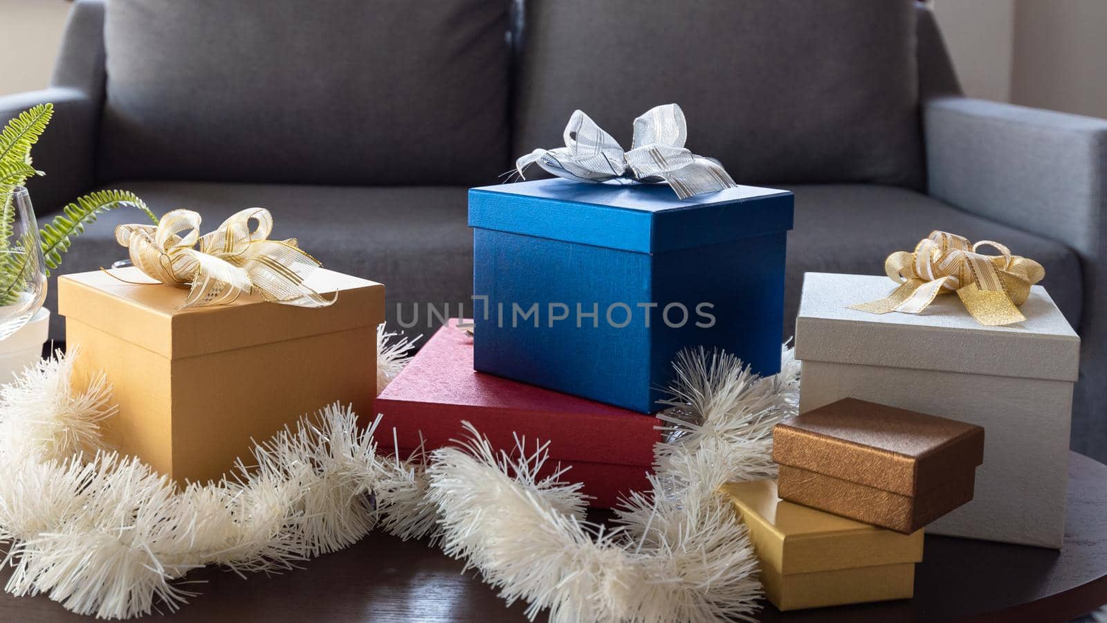 Beautiful Christmas gift boxes wrapped in colourful paper with ribbon bow on table in living room at home by Nuamfolio