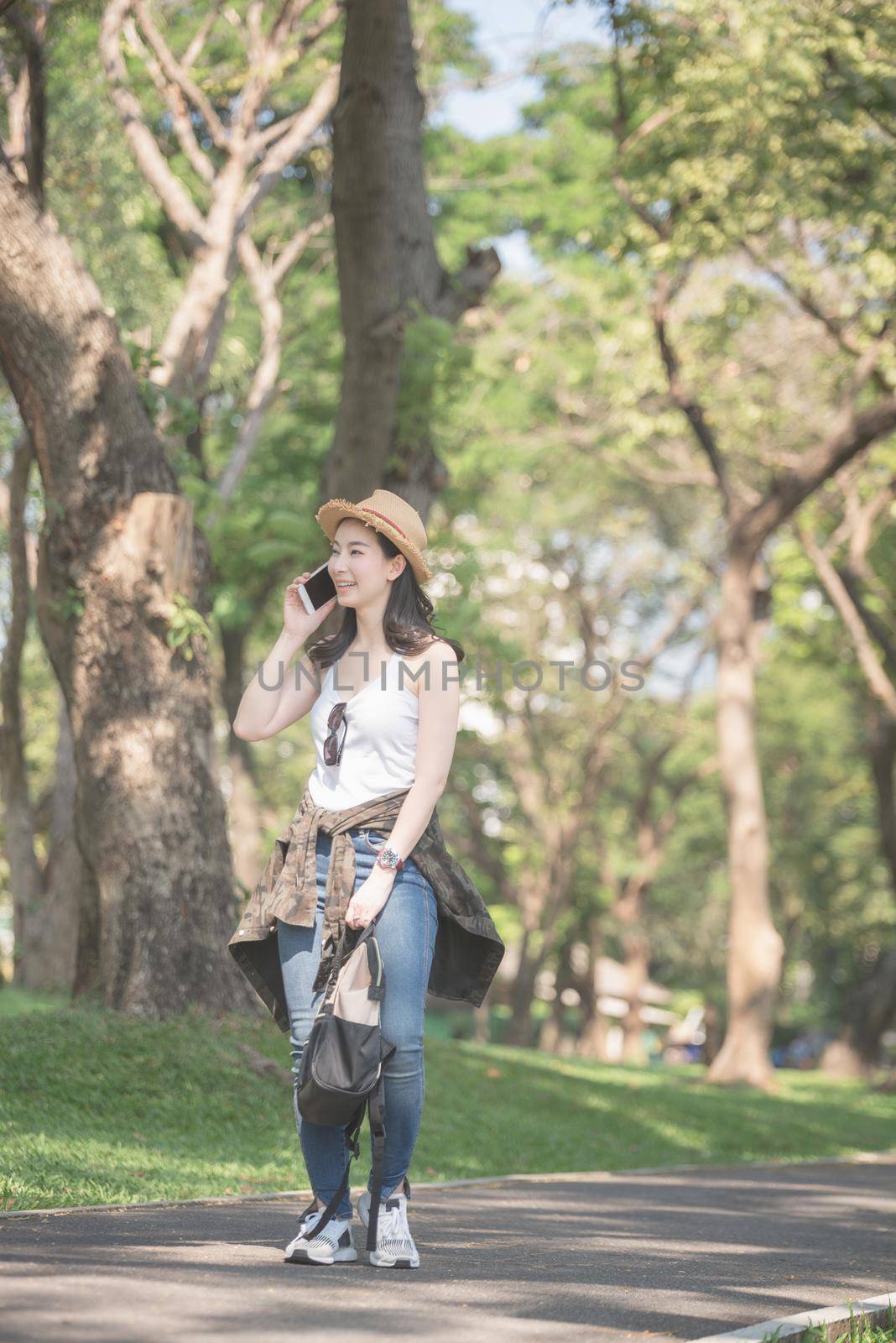Beautiful asian solo tourist woman  smiling and enjoy taking via mobile phone while walking in public nature park. by Nuamfolio