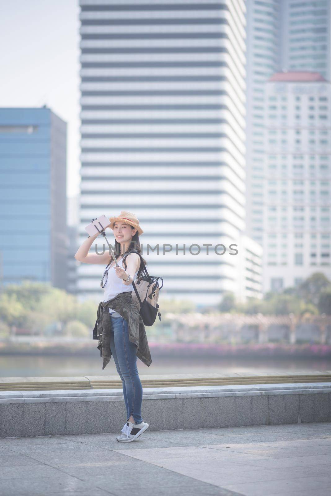 Beautiful asian solo tourist woman taking selfies on a smartphone in urban city downtown. Vacation travel in summer.