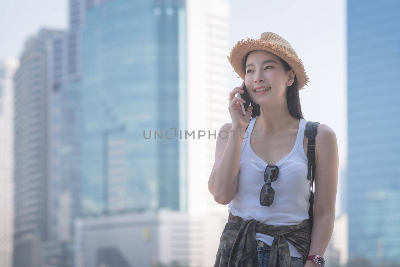 Beautiful asian solo tourist woman smiling and enjoy taking via mobile phone in city downtown. Vacation travel in summer.