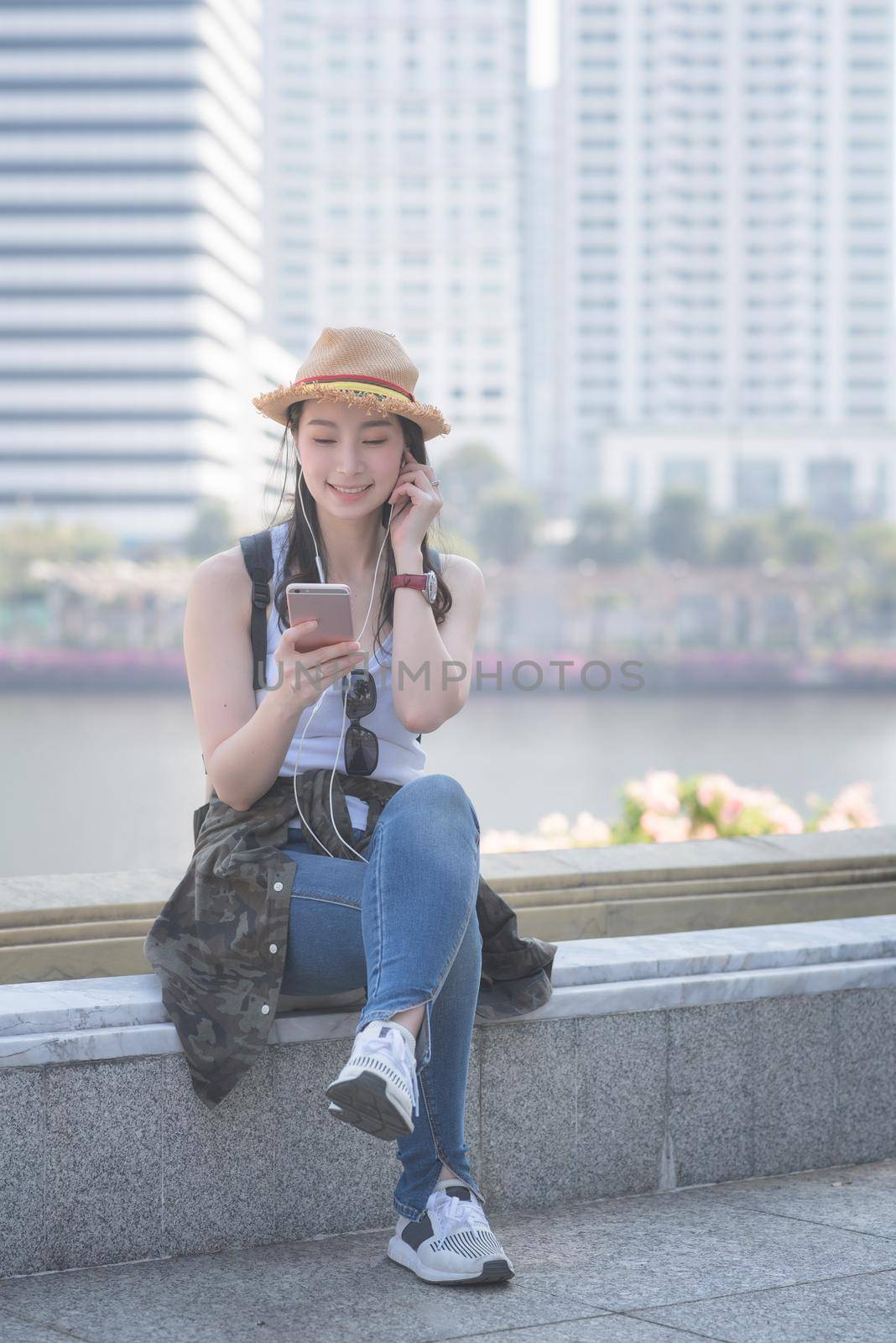 Beautiful asian solo tourist woman relaxing and enjoying listening the music on a smartphone in urban city downtown. by Nuamfolio