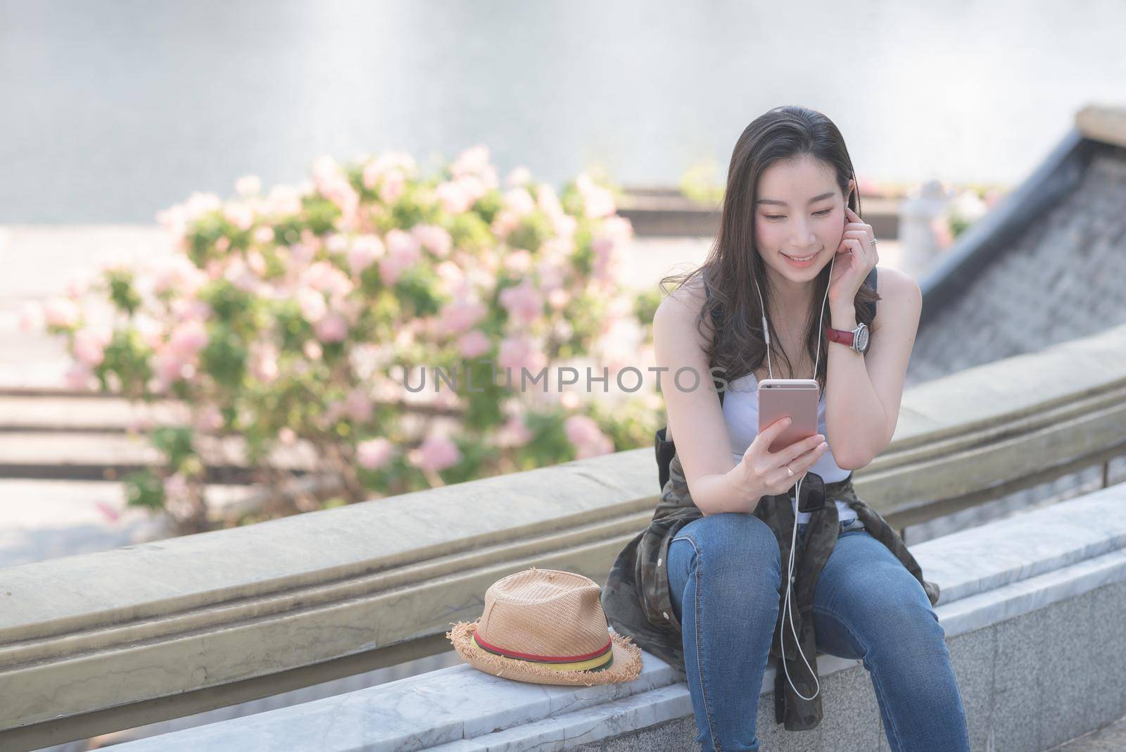 Beautiful asian solo tourist woman relaxing and enjoying listening the music on a smartphone in urban city downtown. Vacation travel in summer.