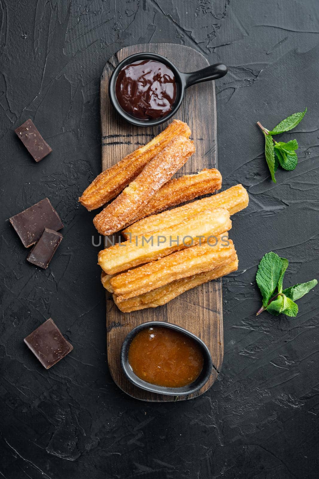 Typical Spanish snack churros, fried-dough pastry served usually with chocolate caramel hot sauce set, on black background, top view flat lay
