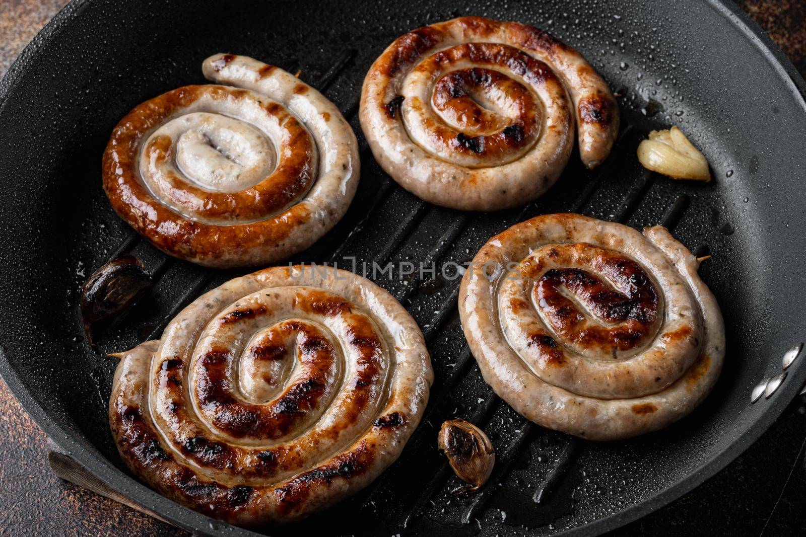 Fried Bavarian pork meat spiral sausages set in cast iron frying pan, on old dark rustic background