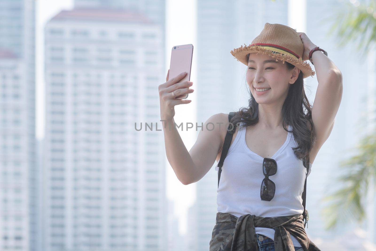 Beautiful asian tourist woman taking selfies on a smartphone in urban city downtown by Nuamfolio