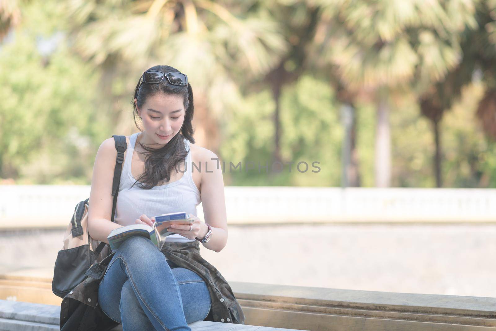 Beautiful asian tourist woman reading the travel guide book searching for for tourists sightseeing spot. Vacation travel in summer.