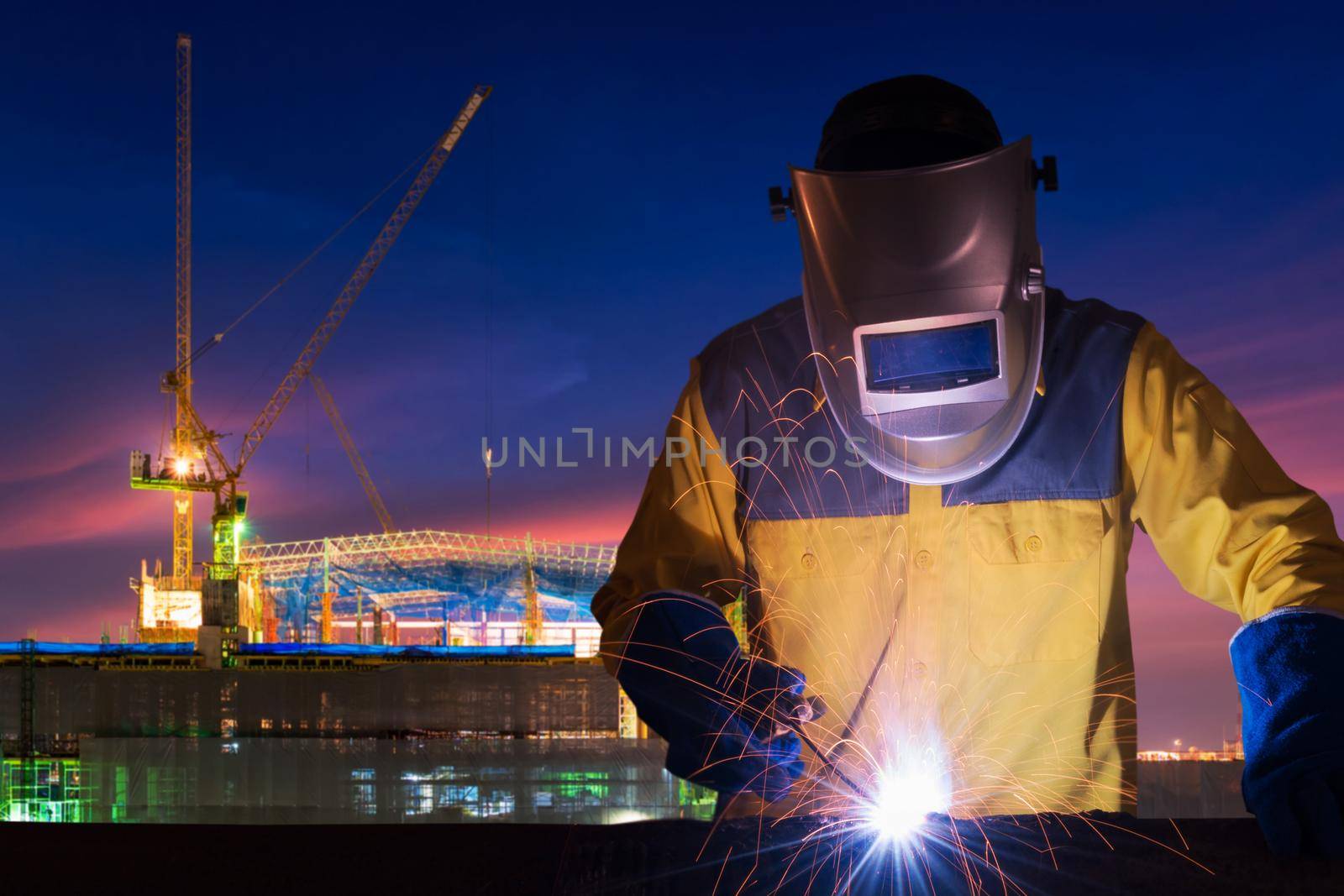 Industrial worker welding steel structure for infrastructure building project with construction site in background. by Nuamfolio