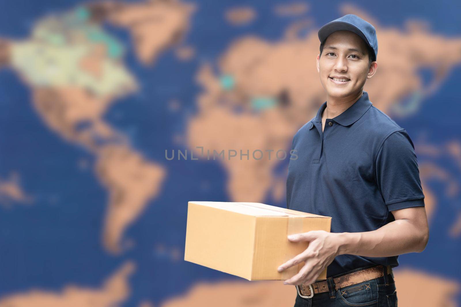 Asian delivery man holding a cardboard box with global map in background for e-commerce and logistics concept.