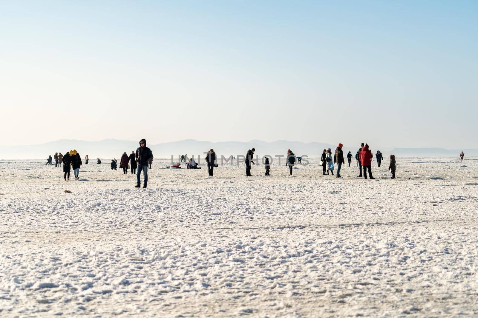 VLADIVOSTOK, RUSSIA-JANUARY 23, 2021: Winter landscape with a view of the icy surface of the Amur Bay. People walk and fish.