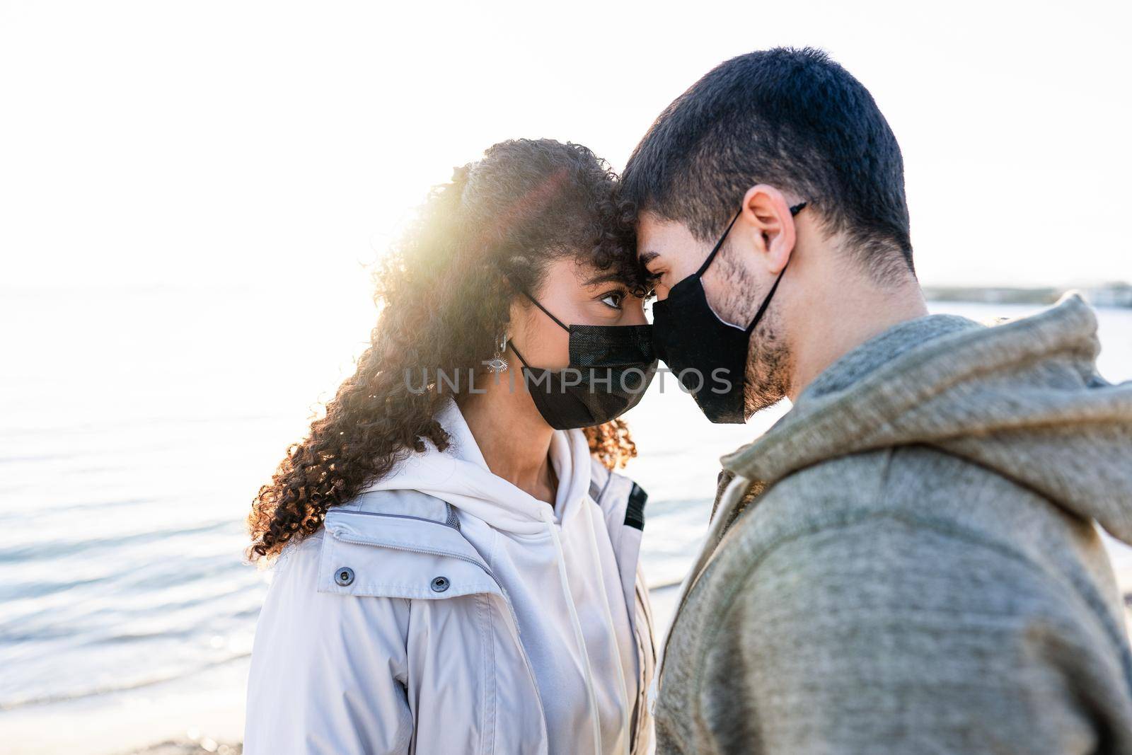 New normal couple in love issues due to social social distancing: man and girlfriend looking in the eyes each other head to head with setting sun reflection on the sea water. Focus on woman eye by robbyfontanesi