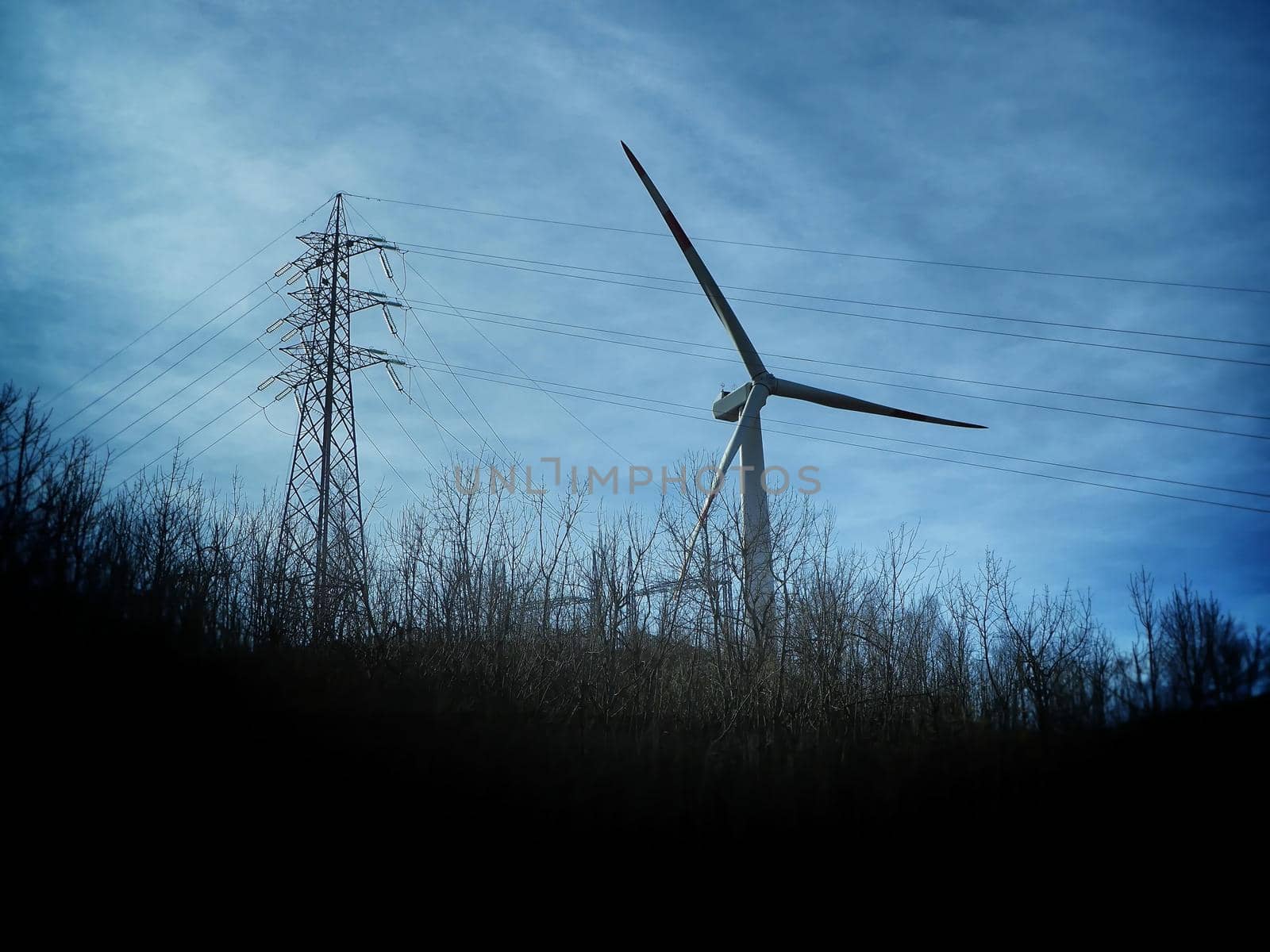 Wind turbine in natural environment near high voltage pylon by lemar