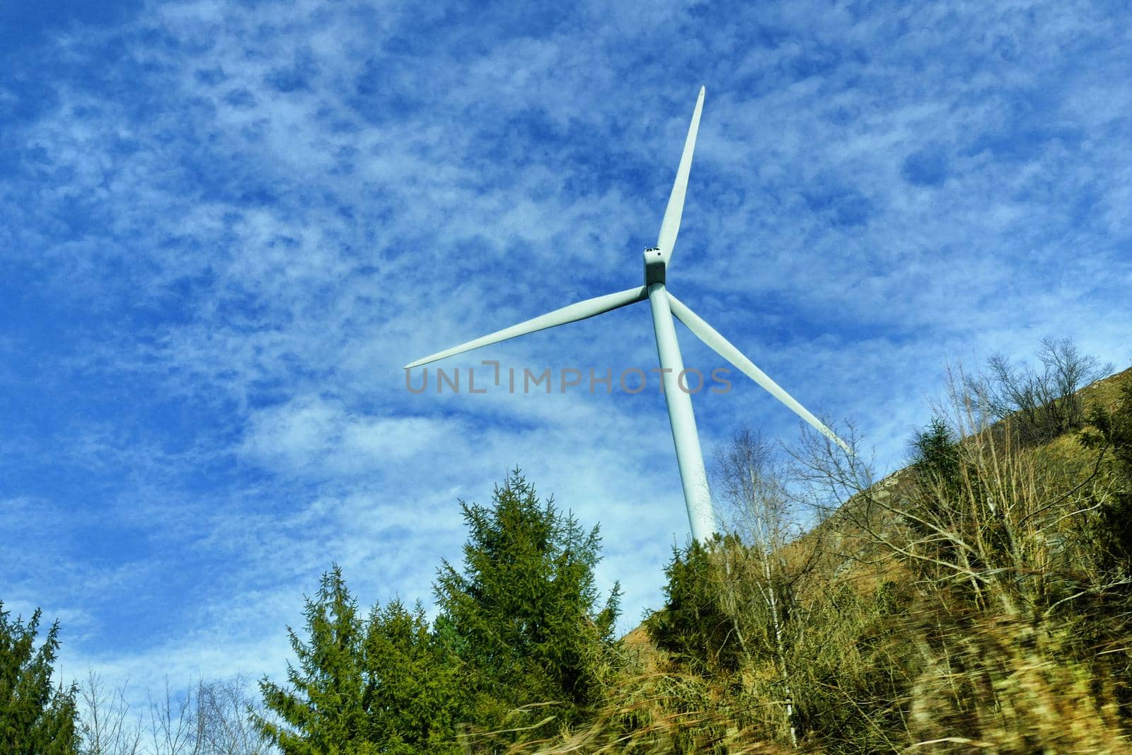 Wind turbine in natural environment near high voltage pylon