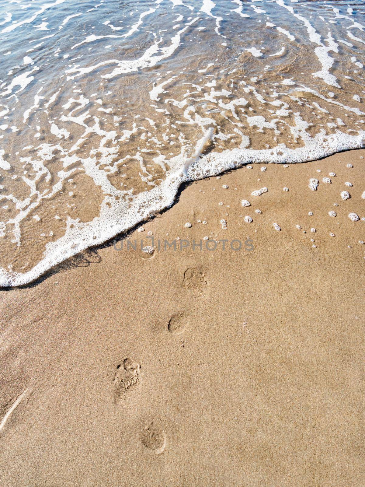 Footprints on wet sand. Sea surf and marks of bare feet. Walking on beach. Leisure activity. Vacation in country with warm climate. Travel.