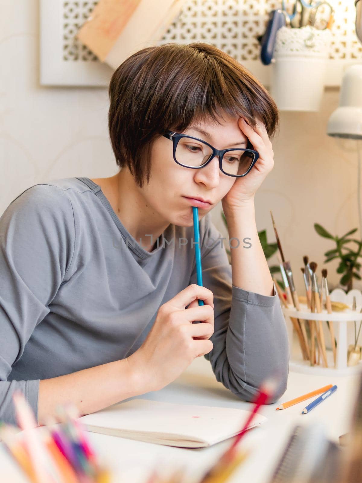 Woman with short hair cut is drawing in notebook. Calming hobby, antistress leisure. Artist at work. Cozy workplace.
