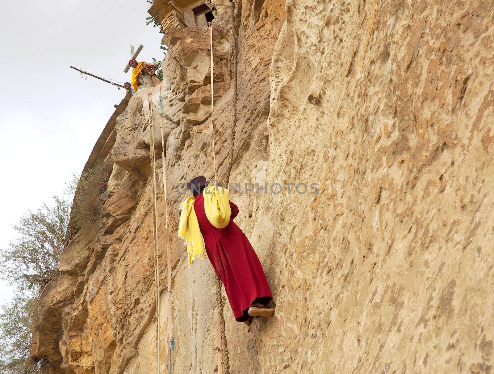 Monk climbing a rock wall at Debre Damo Monastery, Ethiopia by fivepointsix