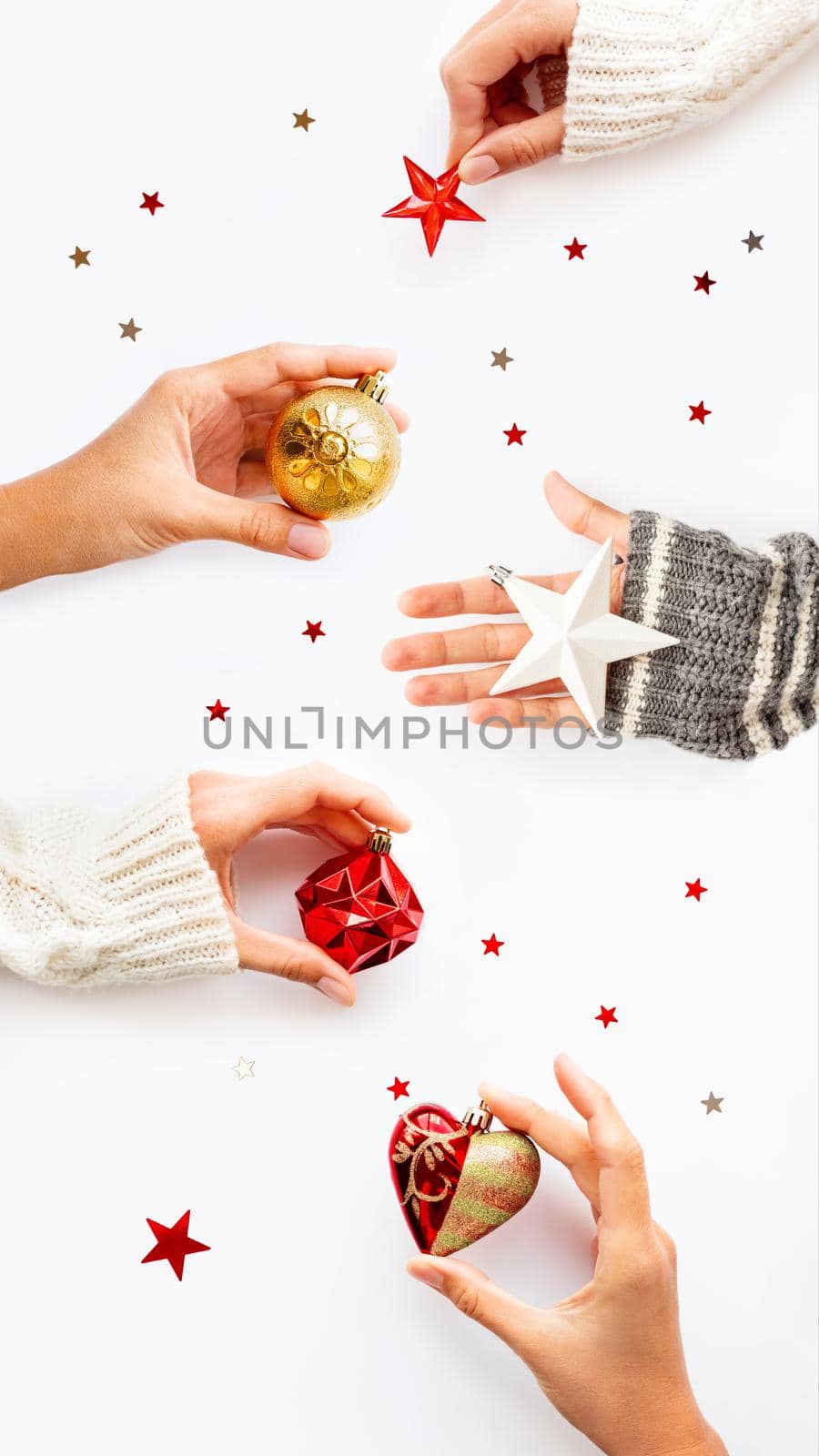 Hands with New Year decoration - red heart, golden ball, white star on white background. Top view on decoration for Christmas tree. Vertical banner 9:16.