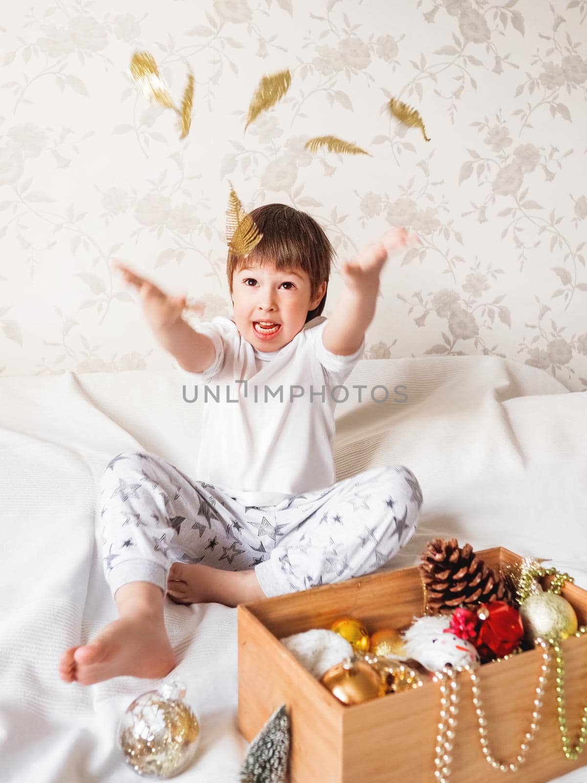 Joyful boy is playing with decorations for Christmas tree. Funny kid is ready for New Year celebration. Cozy home. Winter holiday spirit. by aksenovko