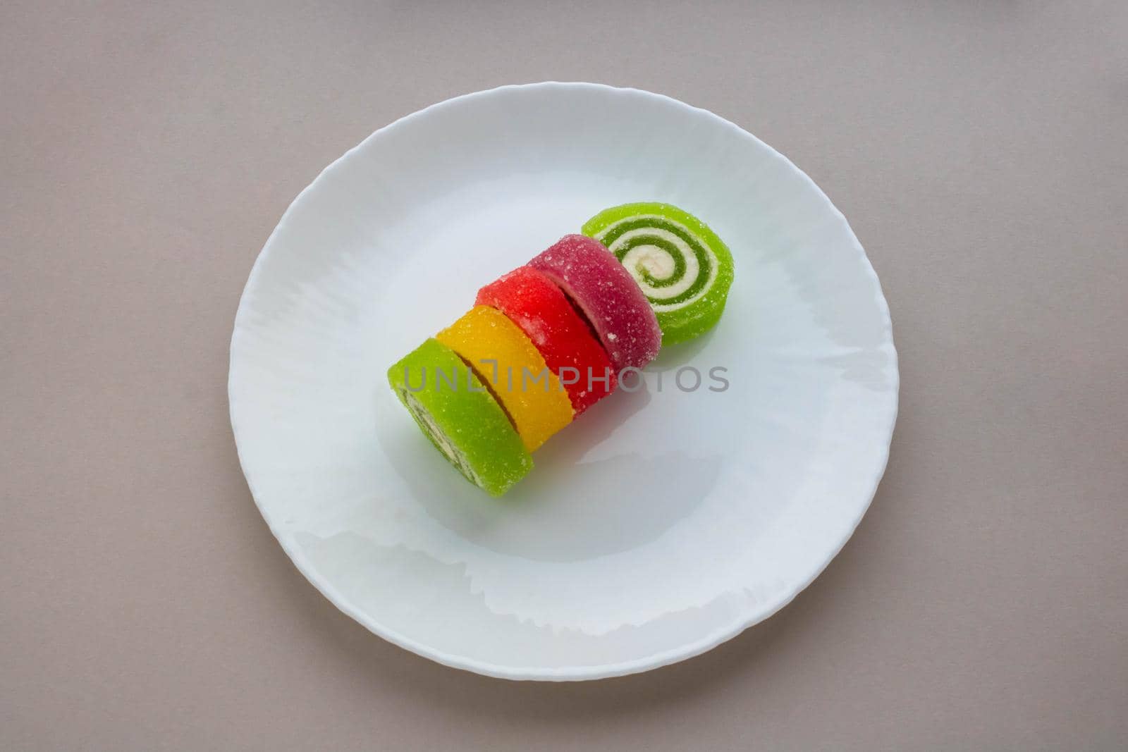 Multicolored spiral marmalade on a white plate on a gray background.