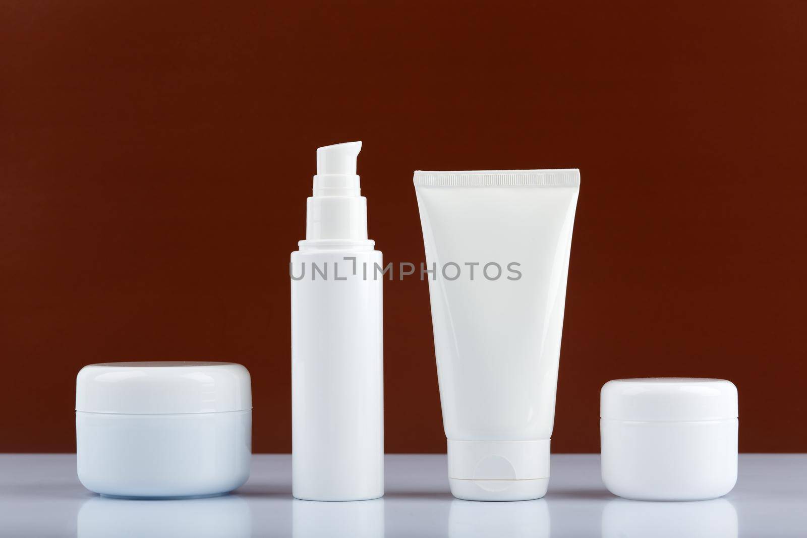 Minimalistic still life with set of beauty products for men on white glossy table against dark brown background. High quality photo