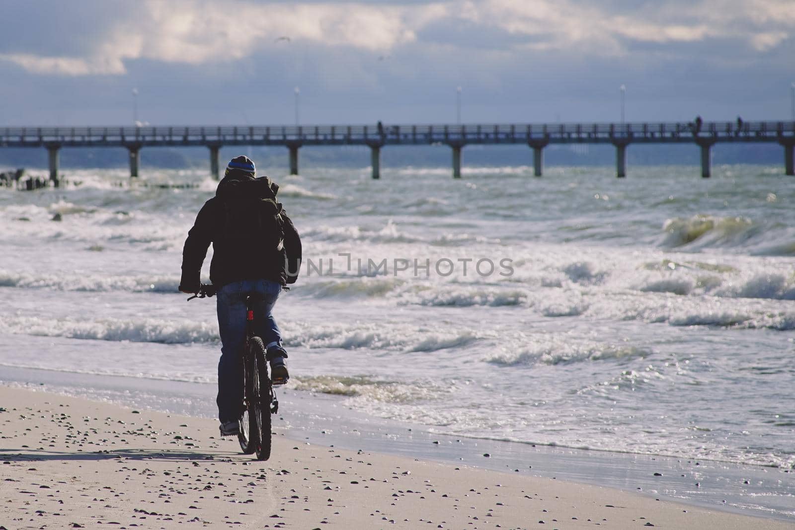 Zelenogradsk, Russia. A lone cyclist in dark clothes rides on a sandy beach towards the pier.