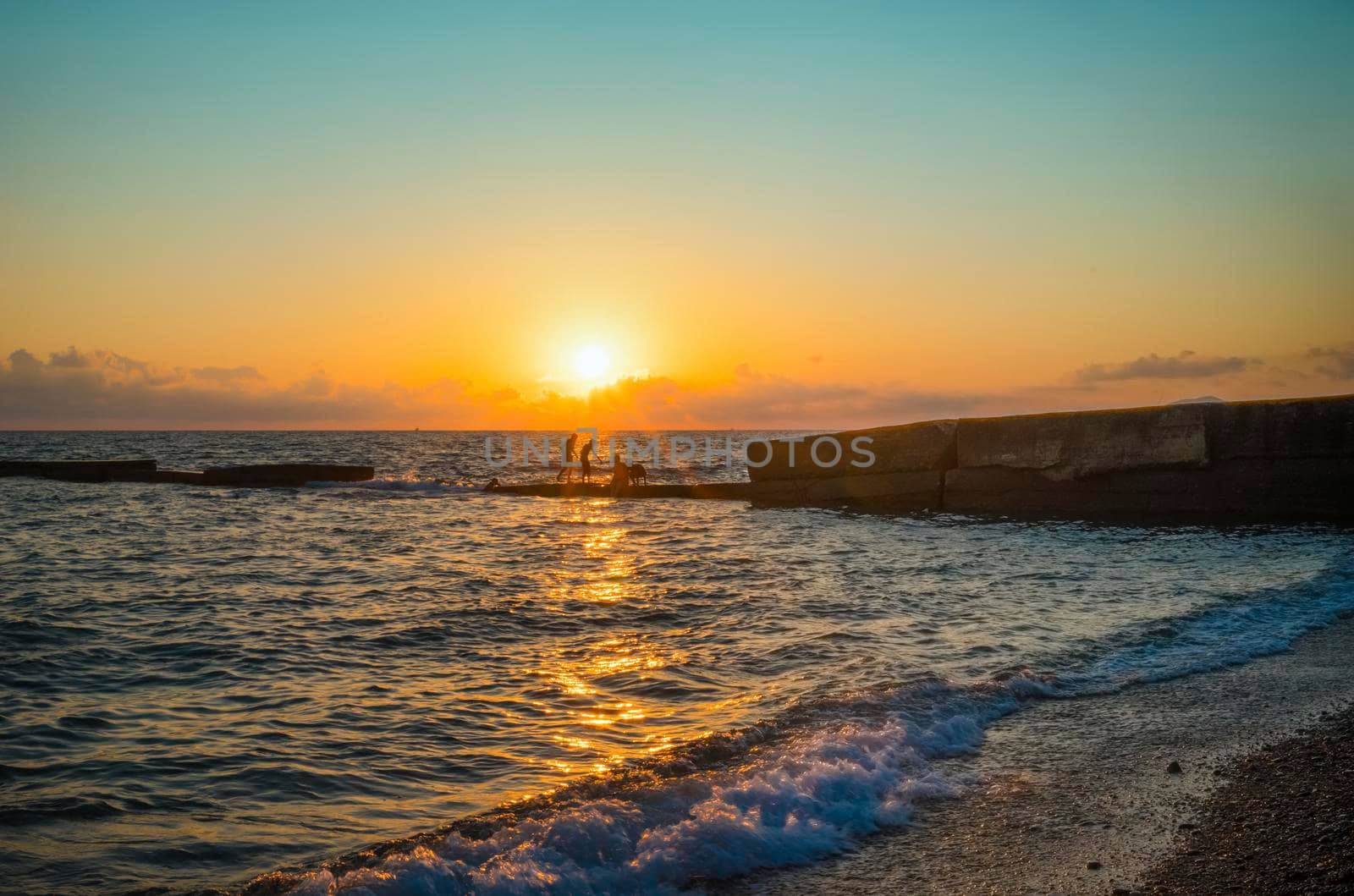 Seascape at sunset with silhouettes of people against the background of sunlight. Sochi, Russia