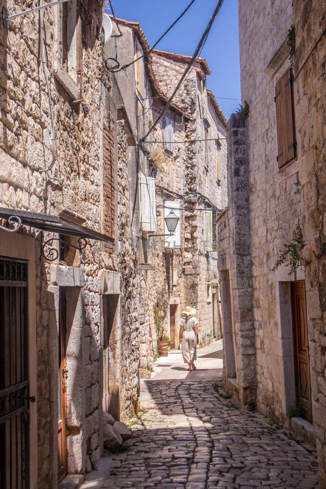 Rear view of beautiful blonde young female traveler wearing straw sun hat sightseeing and enjoying summer vacation in an old traditional costal town at Adriatic cost, Croatia by kasto