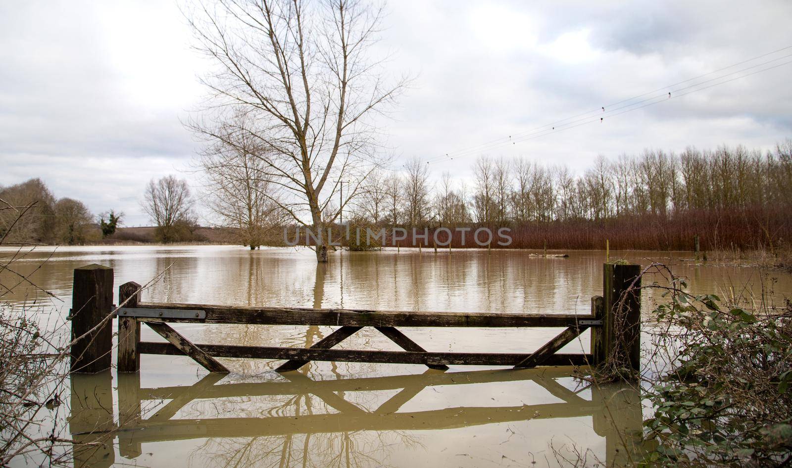 Flooded agricultural farm fields with wooden gate, sky, reflection in water, soaked field. High water in spring, UK, Suffolk spring 2021