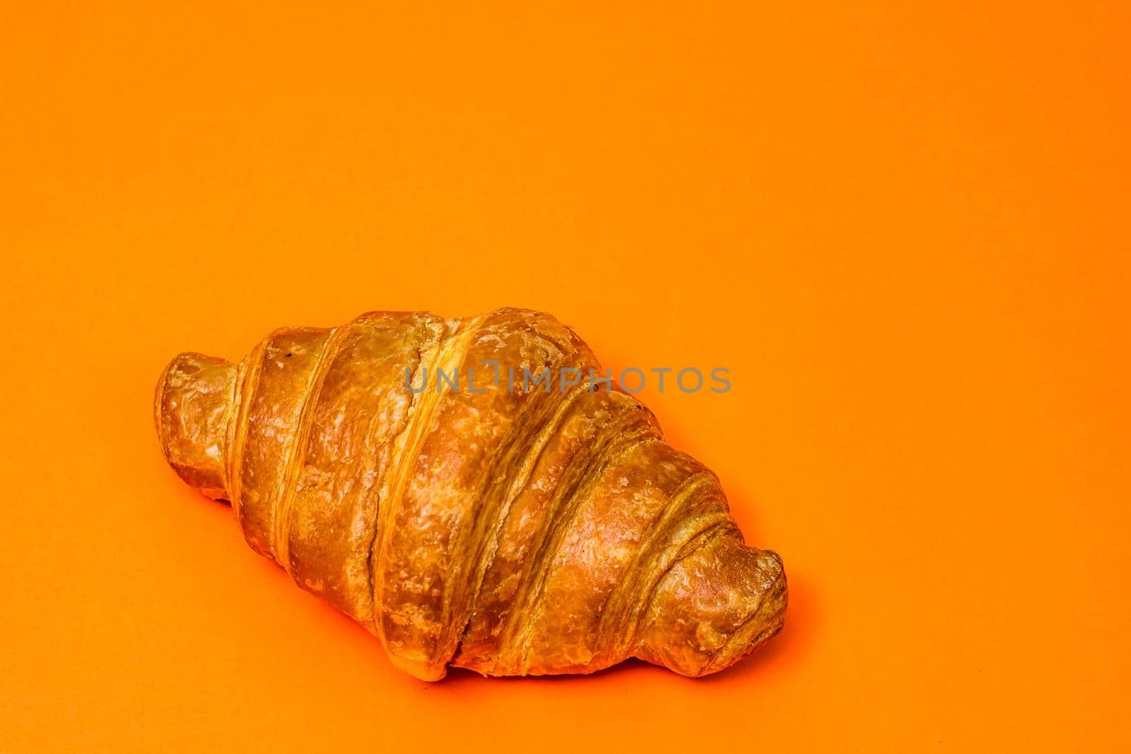 Fresh croissant isolated on orange board. French breakfast concept.