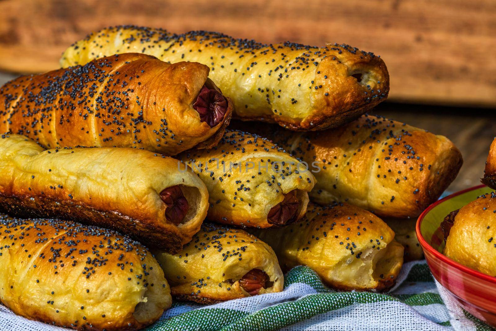 Sausages baked in dough sprinkled with salt and poppy seeds in a rustic composition. Sausages rolls, delicious homemade pastries.