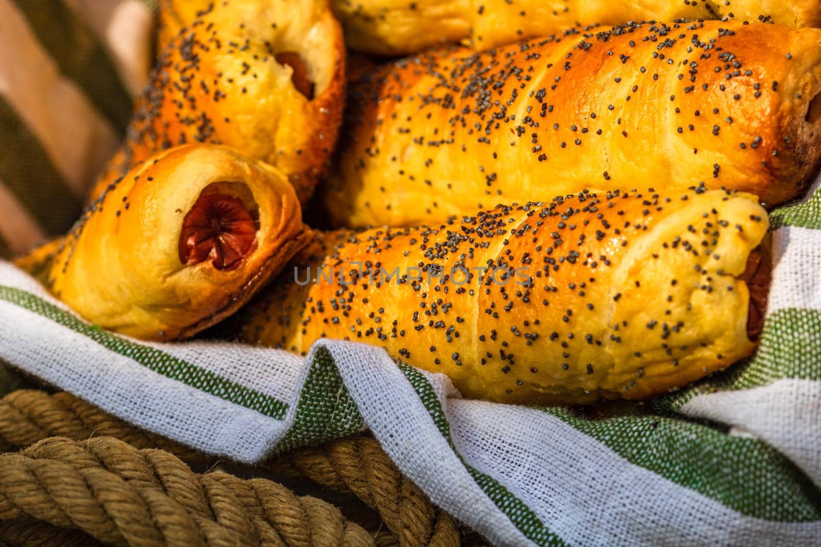 Sausages baked in dough sprinkled with salt and poppy seeds in a rustic basket. Sausages rolls, delicious homemade pastries in a rustic composition.