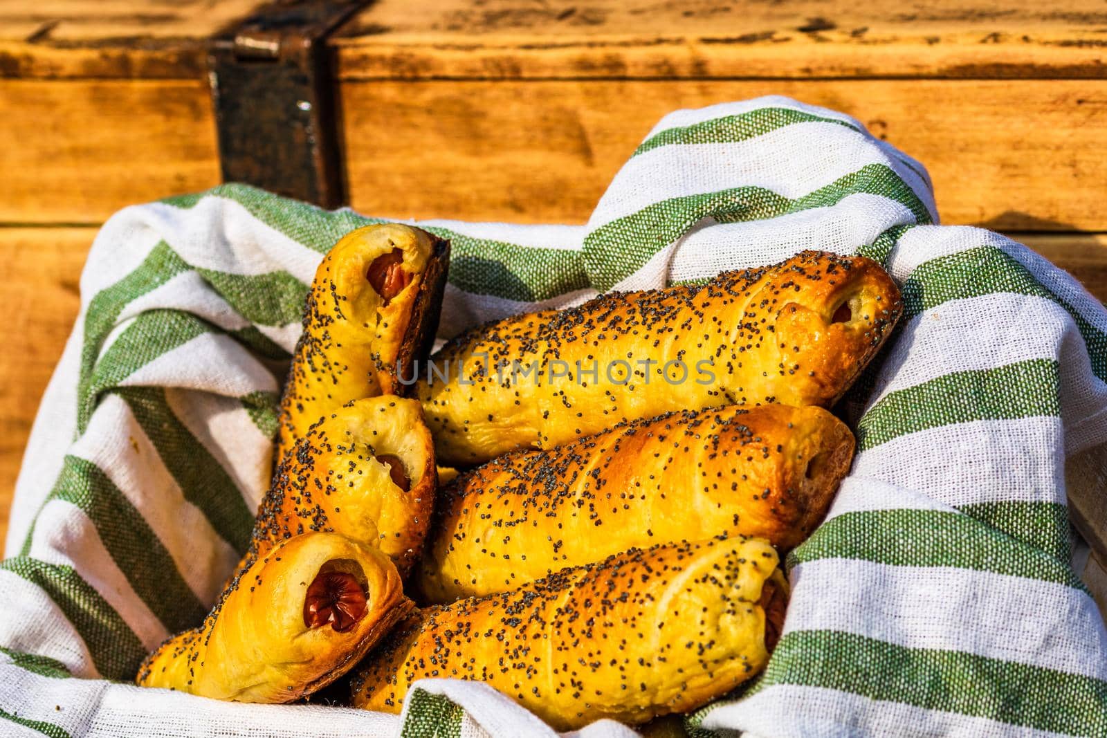 Sausages baked in dough sprinkled with salt and poppy seeds in a rustic basket. Sausages rolls, delicious homemade pastries in a rustic composition.