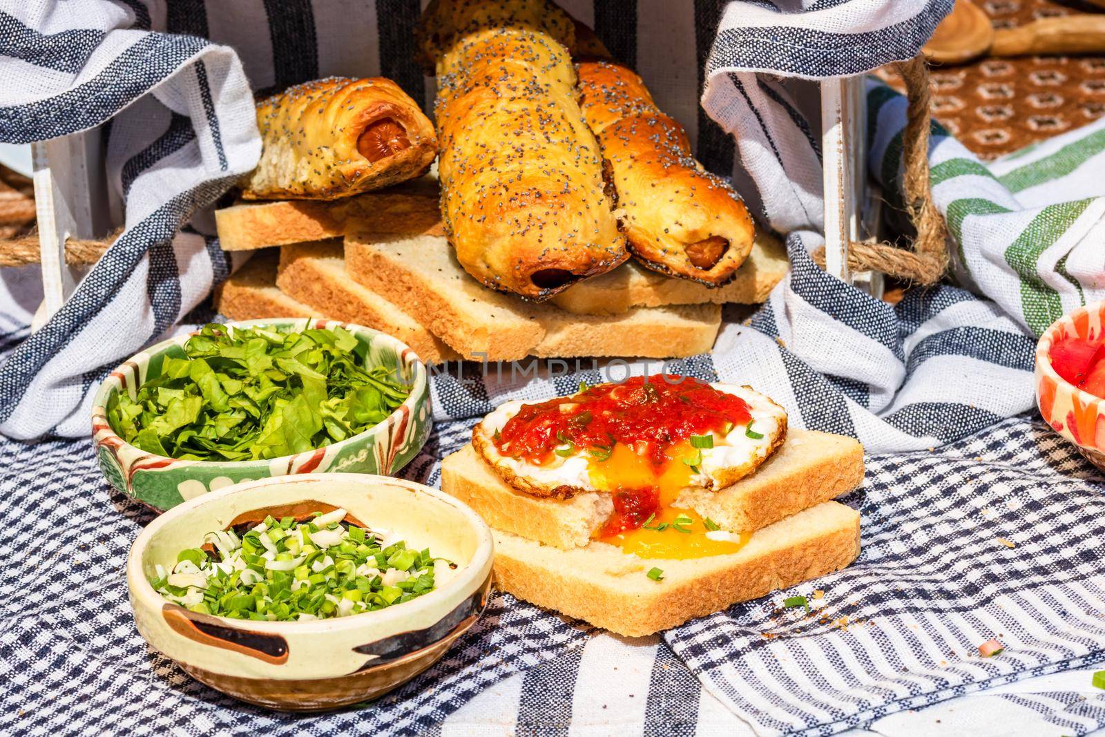 Rustic composition with sausages rolls, fried egg on toast bread, different bowls with sauce and chopped vegetables.