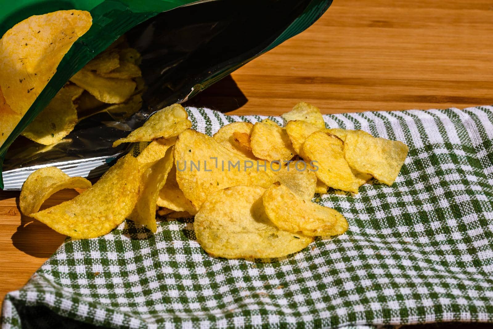 Detail of crispy potato chips on napkin on wooden table. Salted potato chips, junk food concept by vladispas