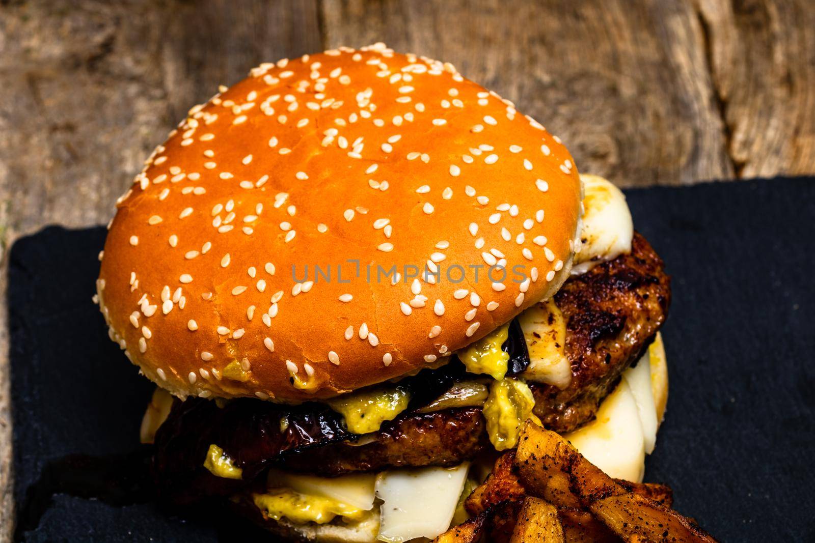 Detail view of fresh tasty cheese burger and fried potatoes on a wooden table