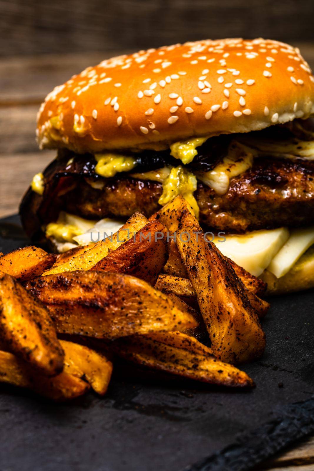 Detail view of fresh tasty cheese burger and fried potatoes on a wooden table